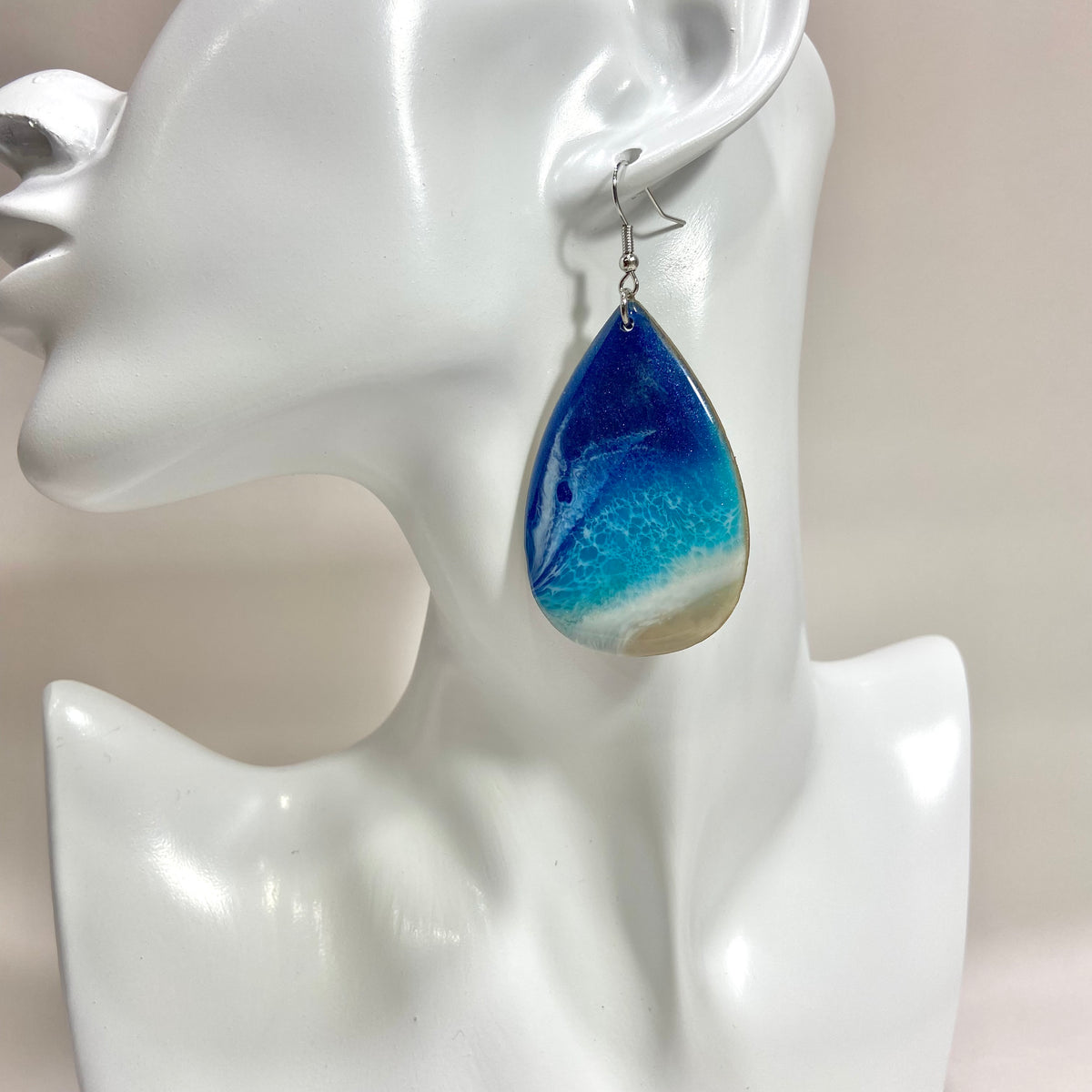 Young woman wearing an ocean Teardrop Earrings by Mamota Creative, handmade resin jewelry with a wooden base.
