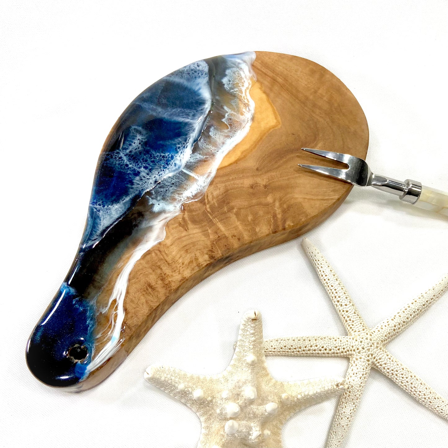 Small olive wood serving board with blue ocean wave resin art and natural wood grain.