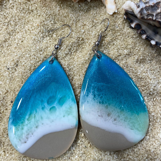 Close-up of ocean-inspired resin teardrop earrings with a wooden base by Mamota Creative.