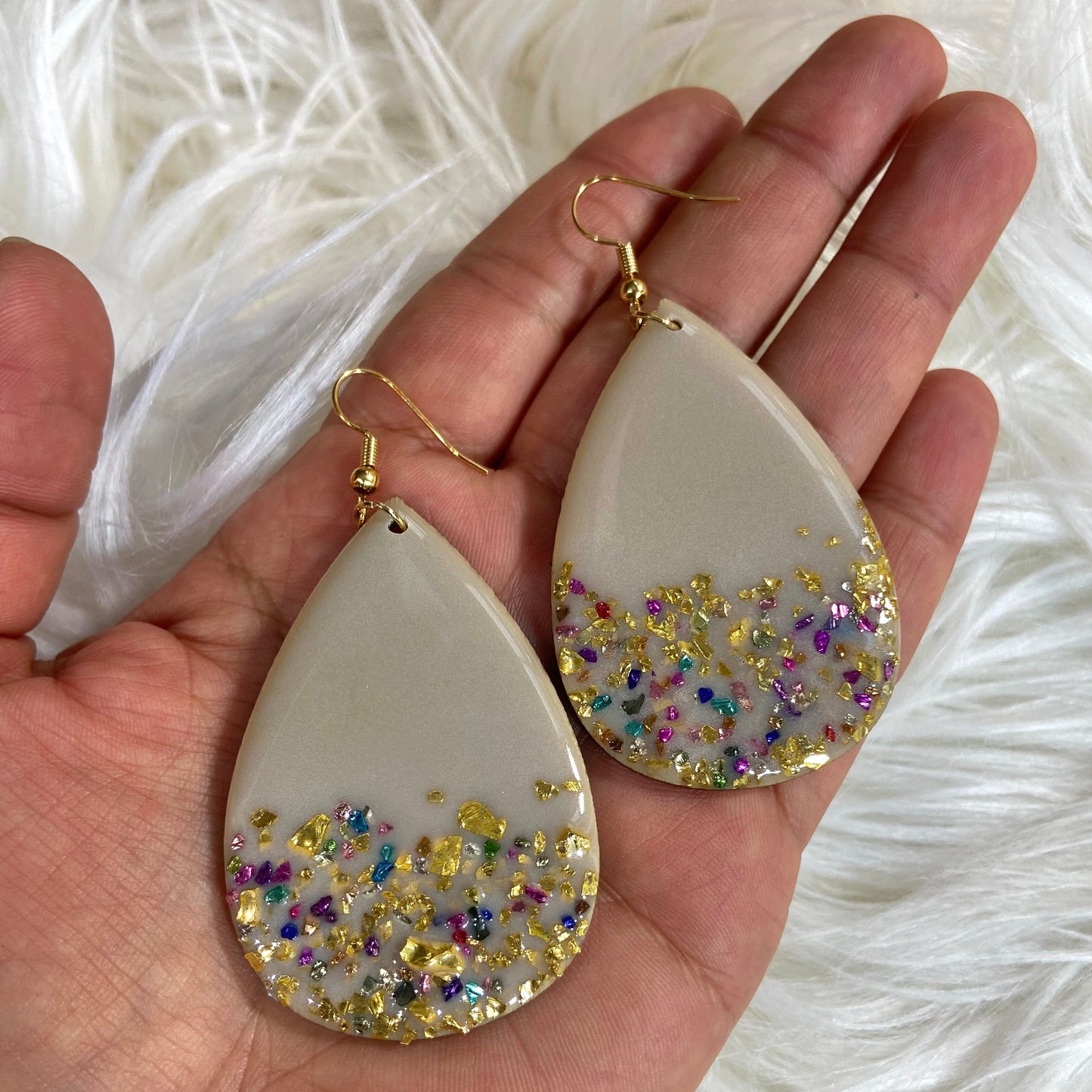 Close-up of tan teardrop resin earrings showing colorful glass chip accents