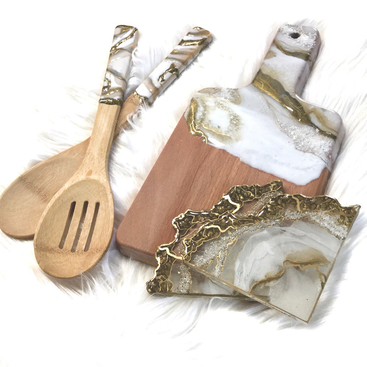 Set of white-gold marble serving board with matching coasters and pair of wooden spoons on white surface.