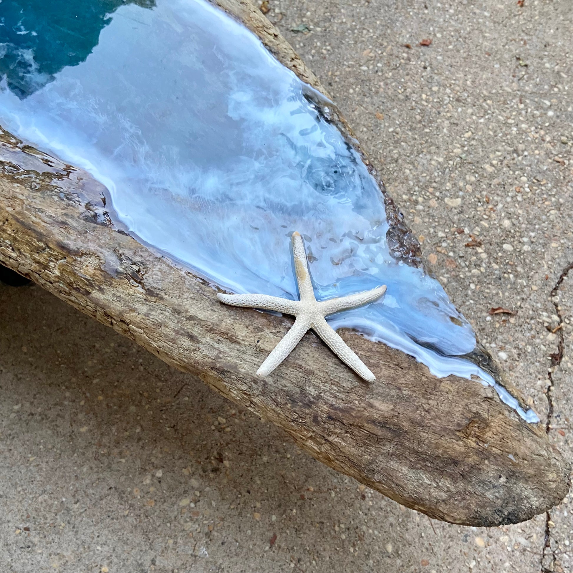 Close up of a partial resin wave on natural drift wood with sea star decoration on a concrete setting