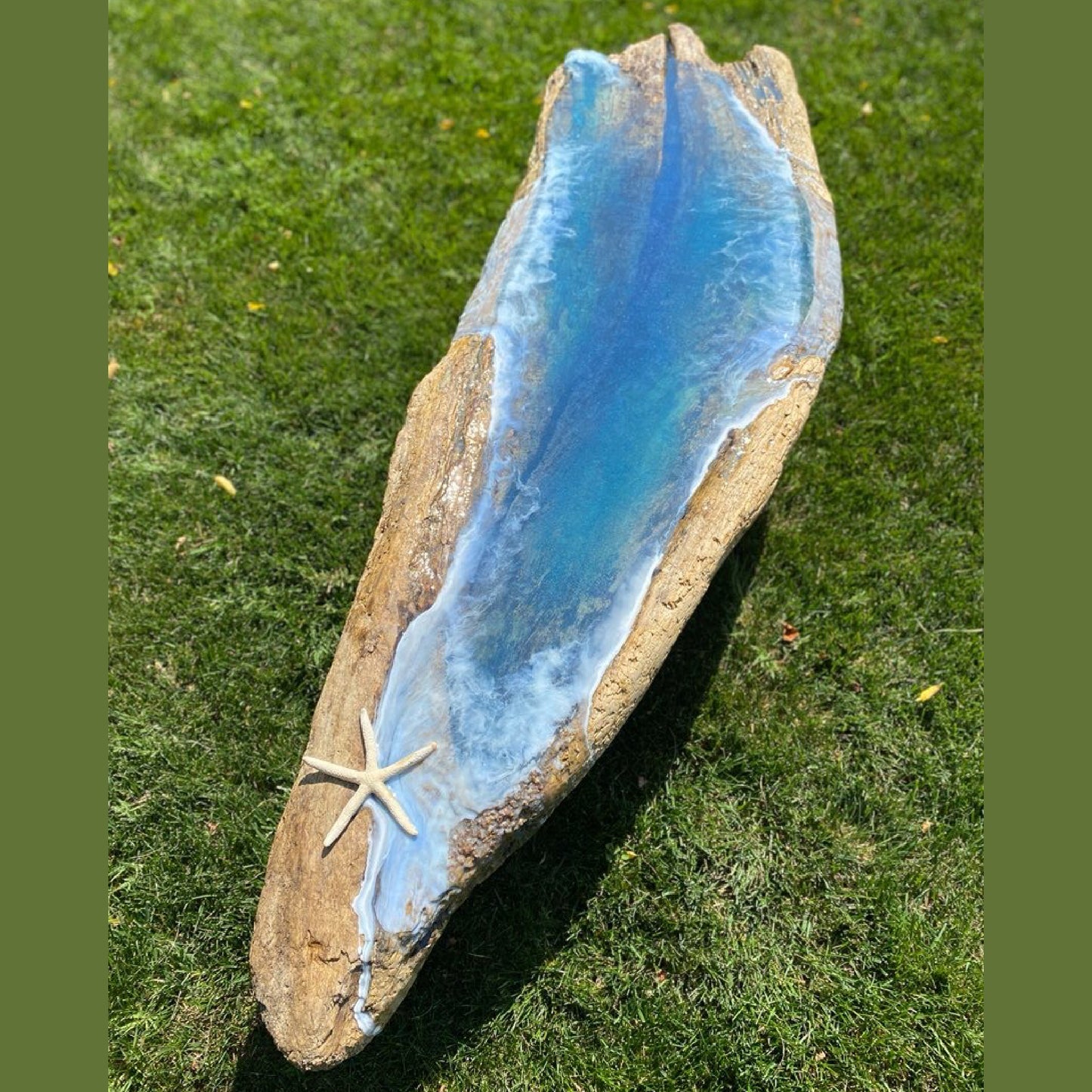 Handcrafted coastal resin coffee table with ocean wave design and sea star accent, displayed outdoors on grass.